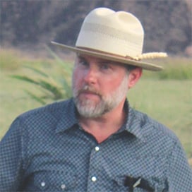 a man wearing a hat standing in a field.