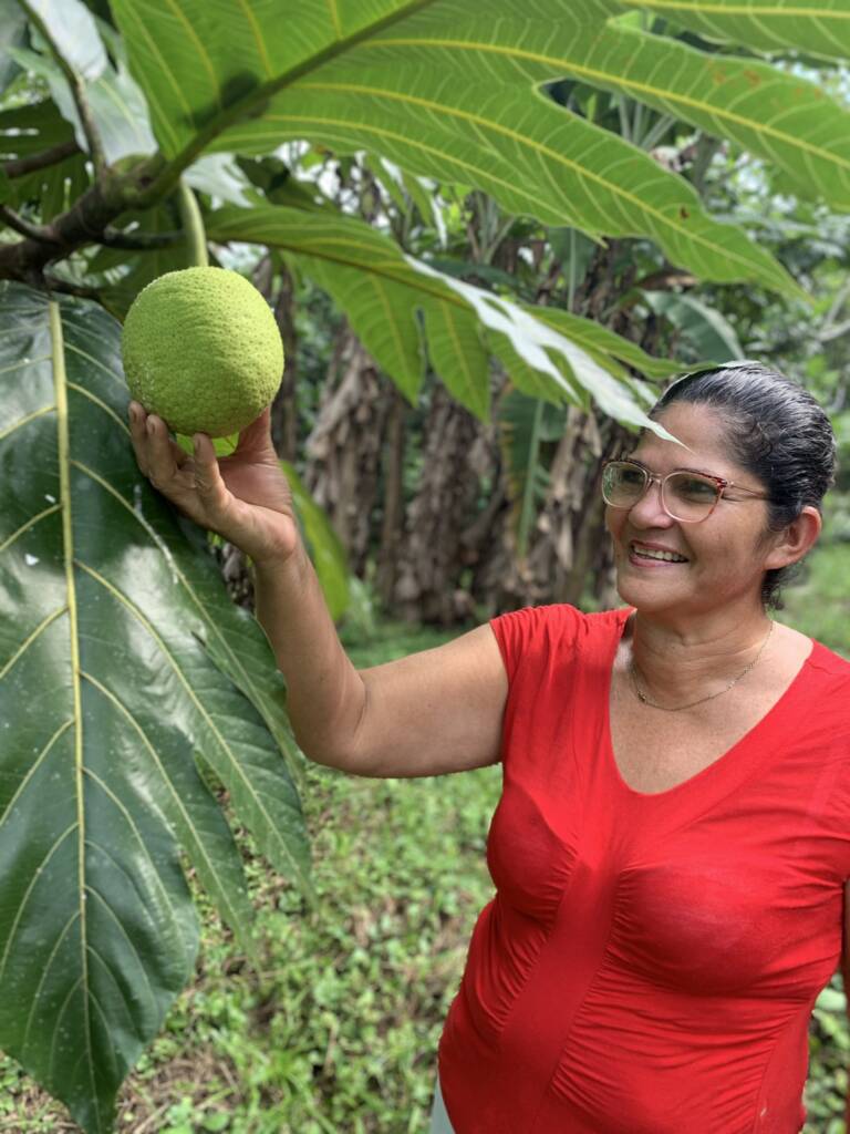 a woman in a red shirt is holding a green fruit.