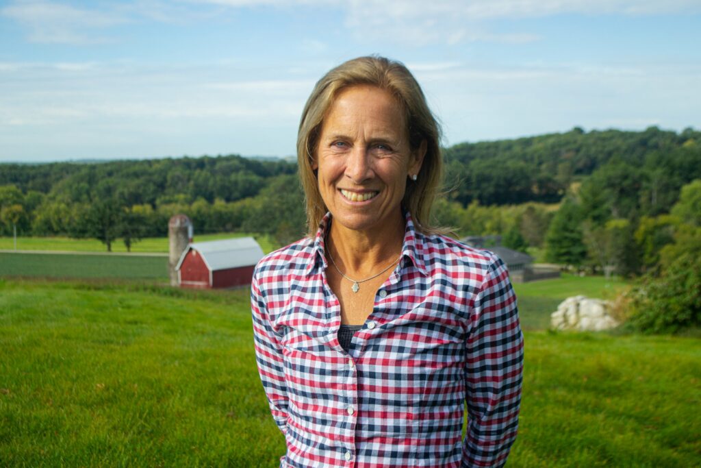 a woman standing in a field with a barn in the background.